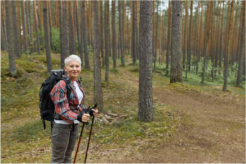 Zdjęcie starszej kobiety z plecakiem i kijkami w lesie